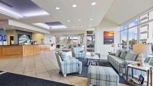 A hotel lobby with a reception desk, seating area with striped sofas, and large windows offering a view. - Perdido Sun 608 with Balcony (Perdido Key)