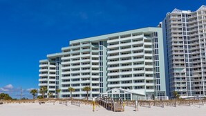 A beachfront hotel with multiple balconies, a beach entrance, and a clear blue sky. - Perdido Sun 608 with Balcony (Perdido Key)
