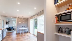 A modern kitchen with a microwave, shelves with jars, and a dining area with a table and chairs. - Re-set, retreat, revive in this beautifully designed little Vermont house. (Sharon)