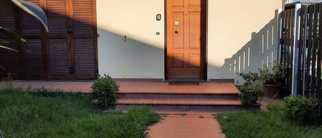 A building with a wooden door, a small porch, and a brick pathway leading to the entrance.