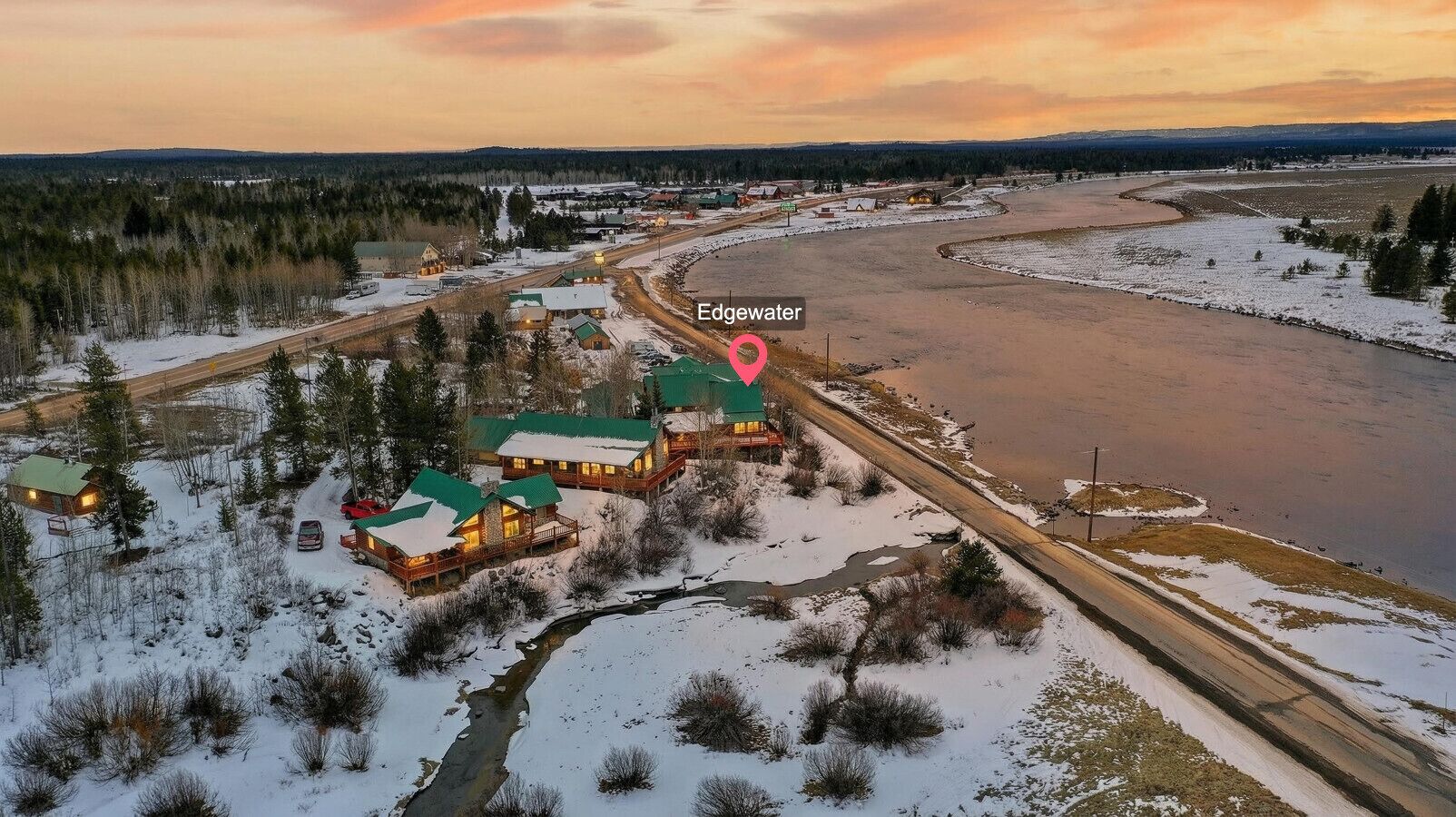 Eine Lodge mit mehreren Gebäuden, einem Fluss und verschneiter Landschaft.