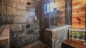Un baño moderno con baldosas de piedra, cabina de ducha de cristal, paredes de madera y un ventanal.