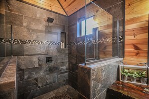 A modern bathroom with stone tiles, a glass shower enclosure, wooden walls, and a small window. - Welcome to Goodnight Moon (Broken Bow)