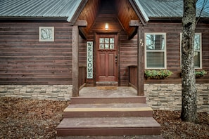 A wooden house with a welcoming sign, a stone foundation, and a tree in the front yard. - Welcome to Goodnight Moon (Broken Bow)