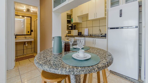 Une cuisine compacte dotée d’un plan de travail en granit, d’un réfrigérateur blanc et d’un coin repas avec une table dressée pour deux personnes.