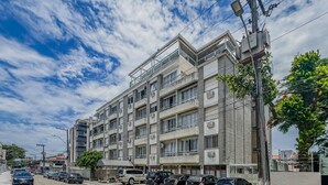 Un immeuble résidentiel à plusieurs étages, doté de balcons, avec des voitures garées devant et un ciel dégagé.