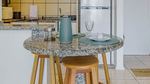 Une cuisine dotée d’un plan de travail en granit, d’une cuisinière, d’un réfrigérateur et d’un coin repas avec des tabourets et une table mise avec un verre, une tasse et un set de table.