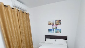 A bedroom with a bed, a nightstand, a wall-mounted air conditioner, and a curtain. - Cosy studio 100m from the sea (Dakar)