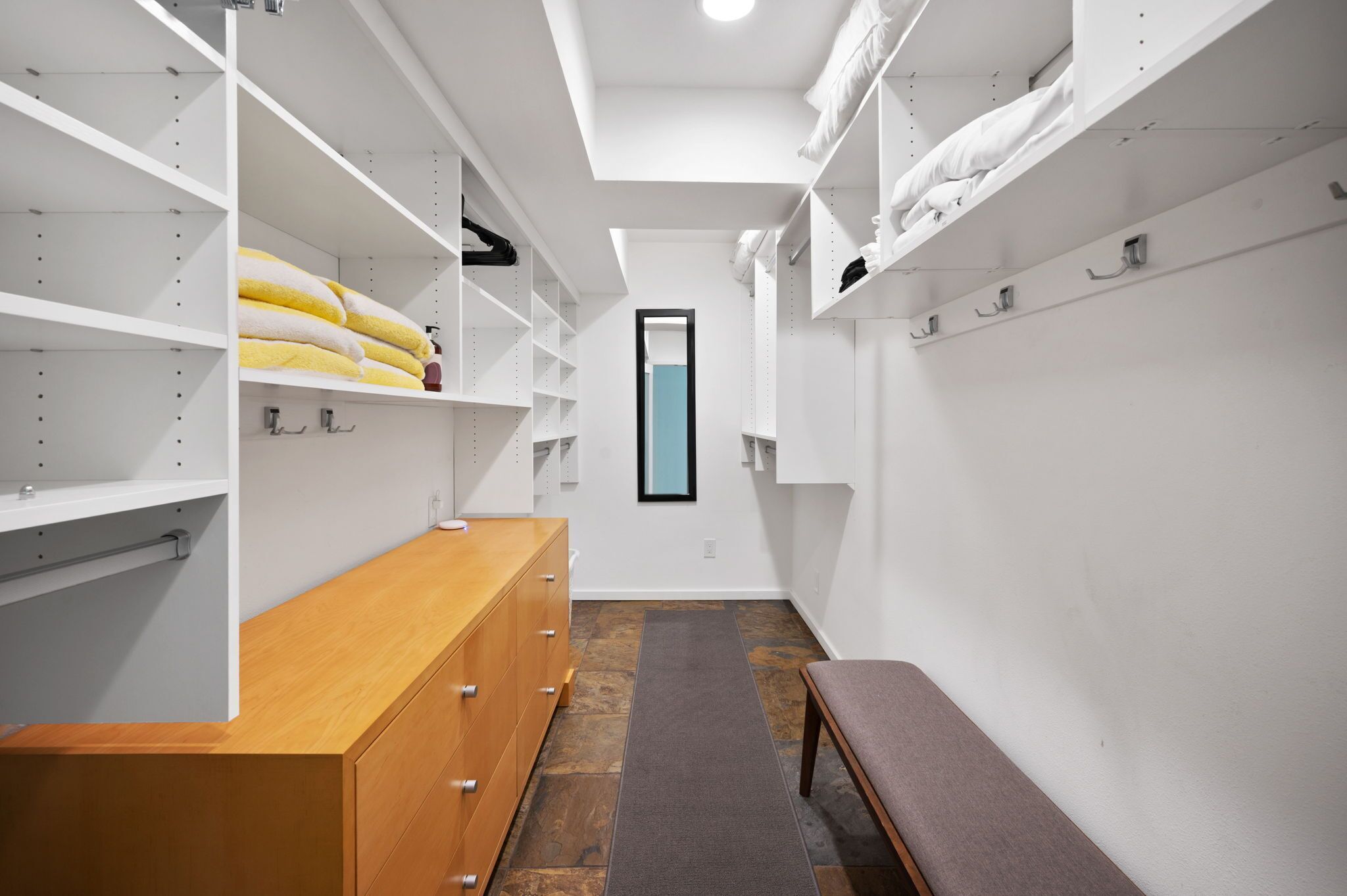A walk-in closet with open shelving, a bench, and a mirror.