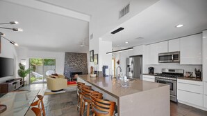 A modern kitchen with a central island, bar stools, and a dining area with a glass table. - Whiskey Rocks 2.0 (Palm Springs)