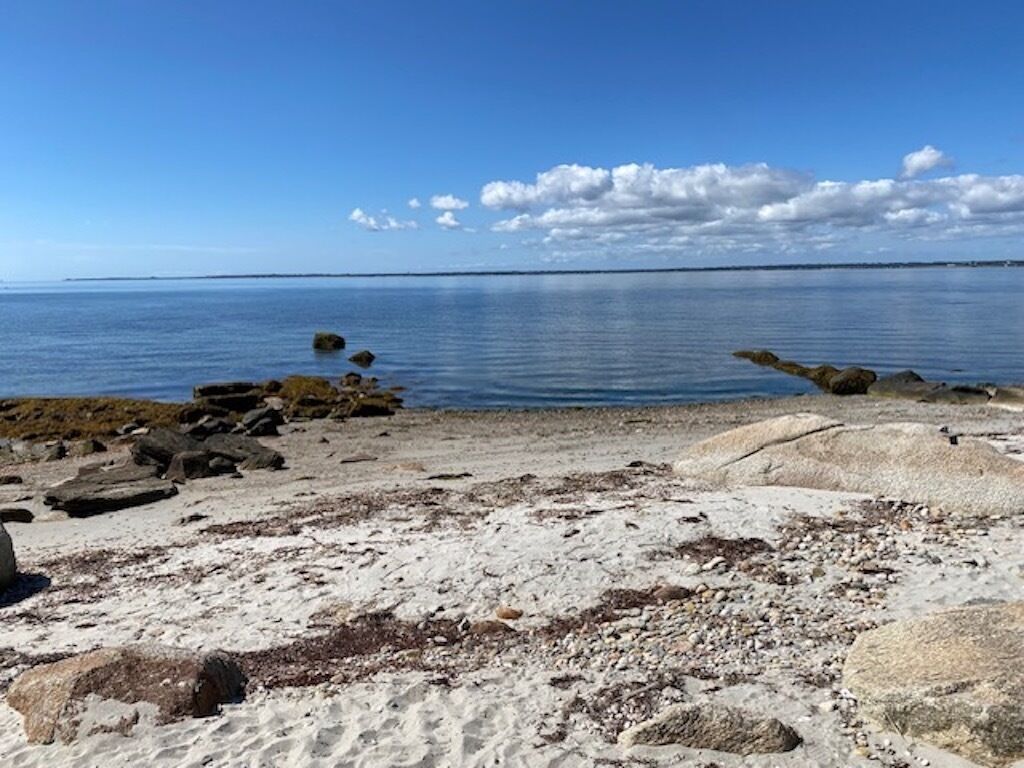 Une plage avec de gros rochers et des galets, un ciel bleu dégagé et une eau calme.
