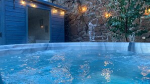 A hot tub with a stone wall and wooden building in the background. - The Manor House (Peel)