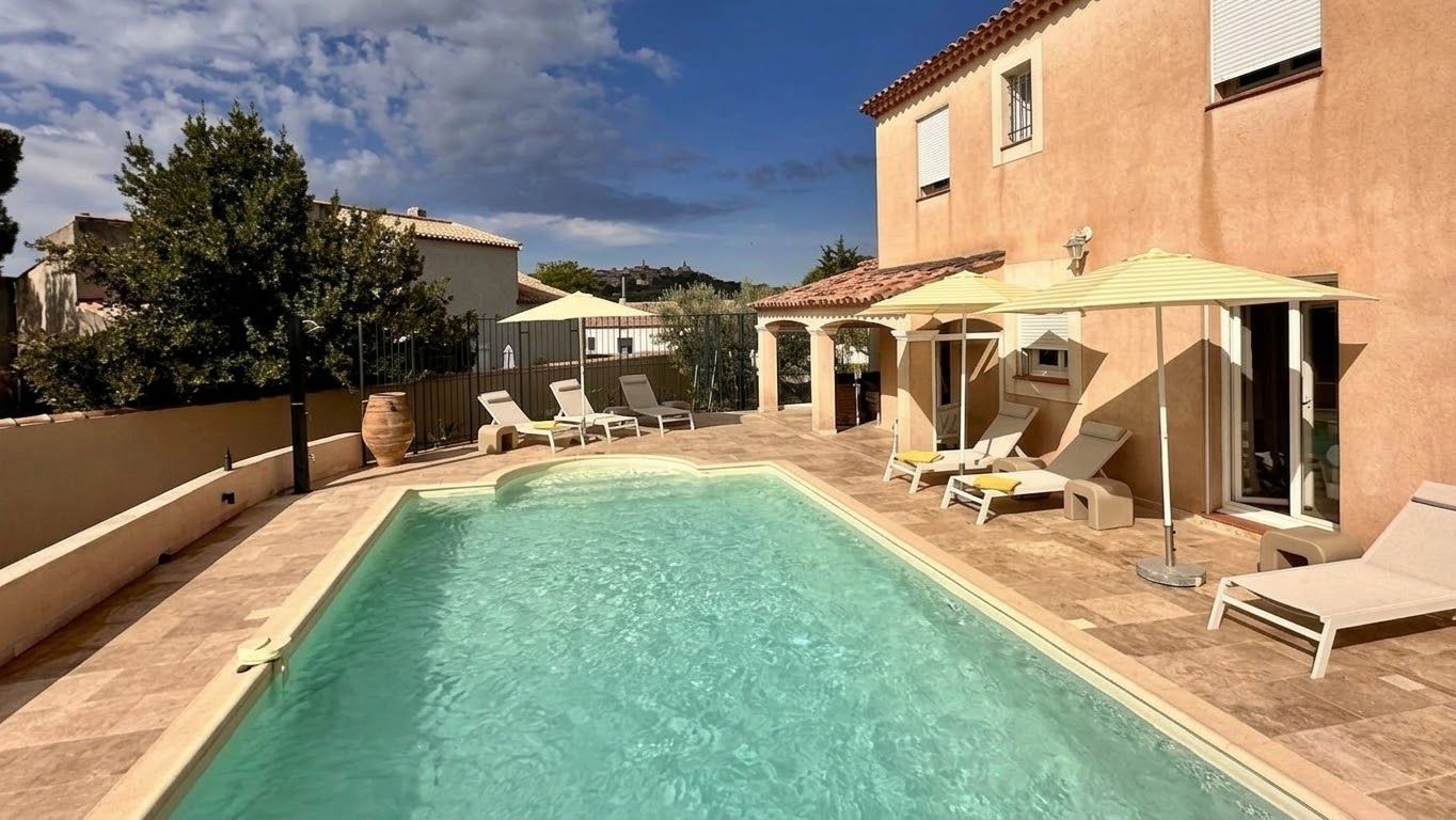A swimming pool with lounge chairs and umbrellas, surrounded by a building with a tiled roof.