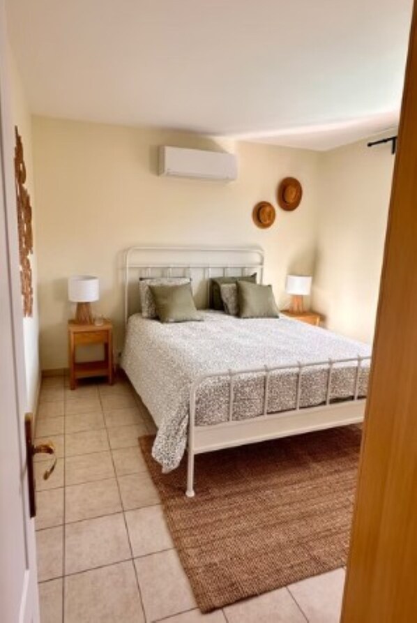 A bedroom with a bed, bedside tables, a wall-mounted air conditioner, and a door. - Beautiful vacation home with enclosed garden and private swimming pool (Regusse)