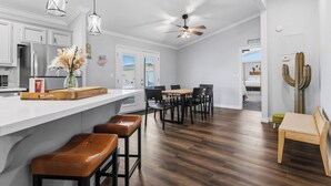 A modern kitchen with white cabinets, a wooden island with bar stools, and a dining area with a table and chairs. - Game On! River Getaway Sleeps 10 in Bullhead City (Bullhead City)