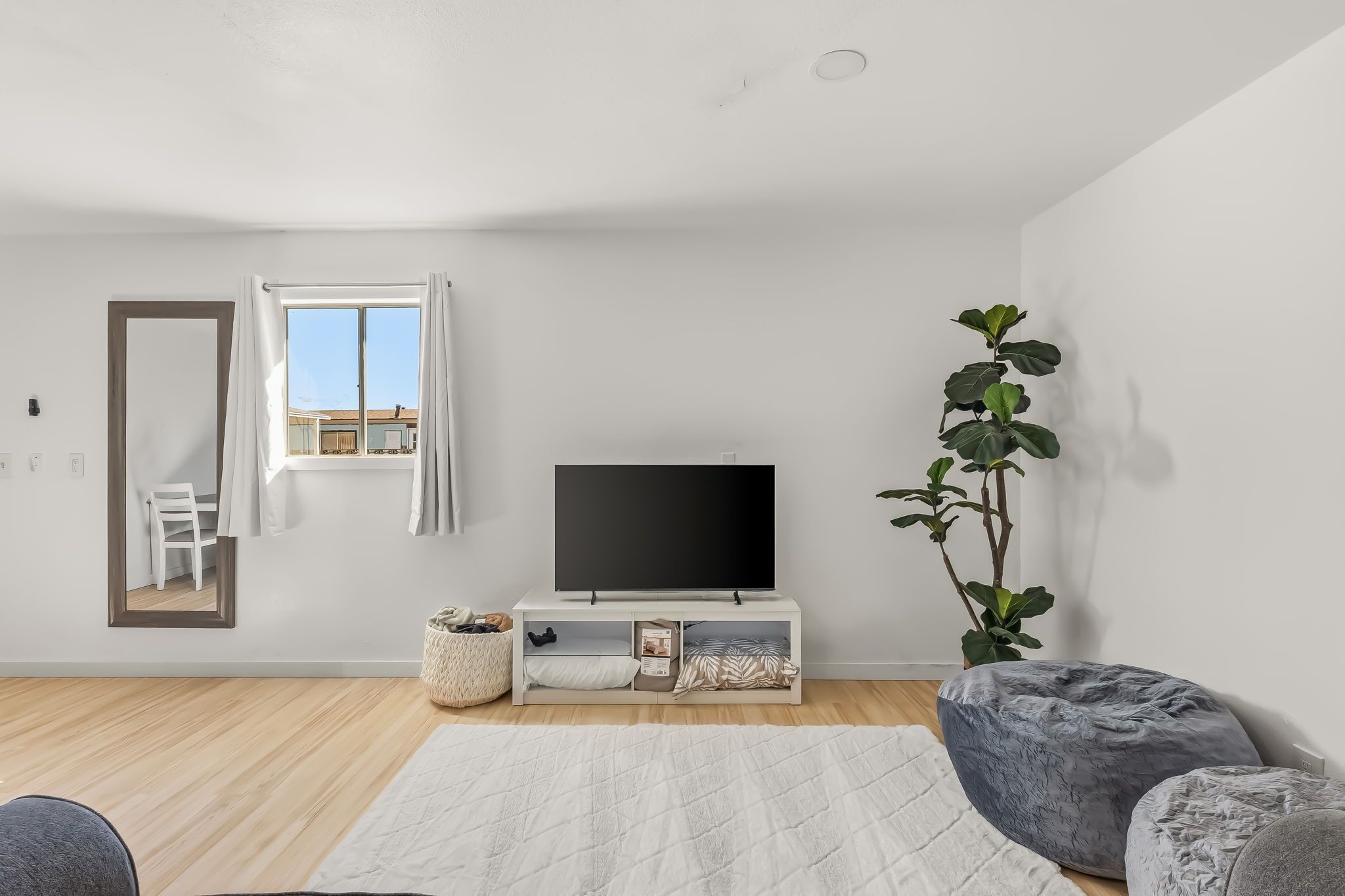 Un salon moderne avec un téléviseur à écran plat, un grand miroir, une plante en pot et un fauteuil poire gris.