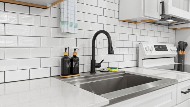 A modern kitchen with white subway tiles, a stainless steel sink, a black faucet, and a white stove.