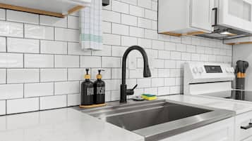 A modern kitchen with white subway tiles, a stainless steel sink, a black faucet, and a white stove.