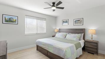 A bedroom with a wooden bed, a ceiling fan, two bedside tables with lamps, and framed pictures on the walls.