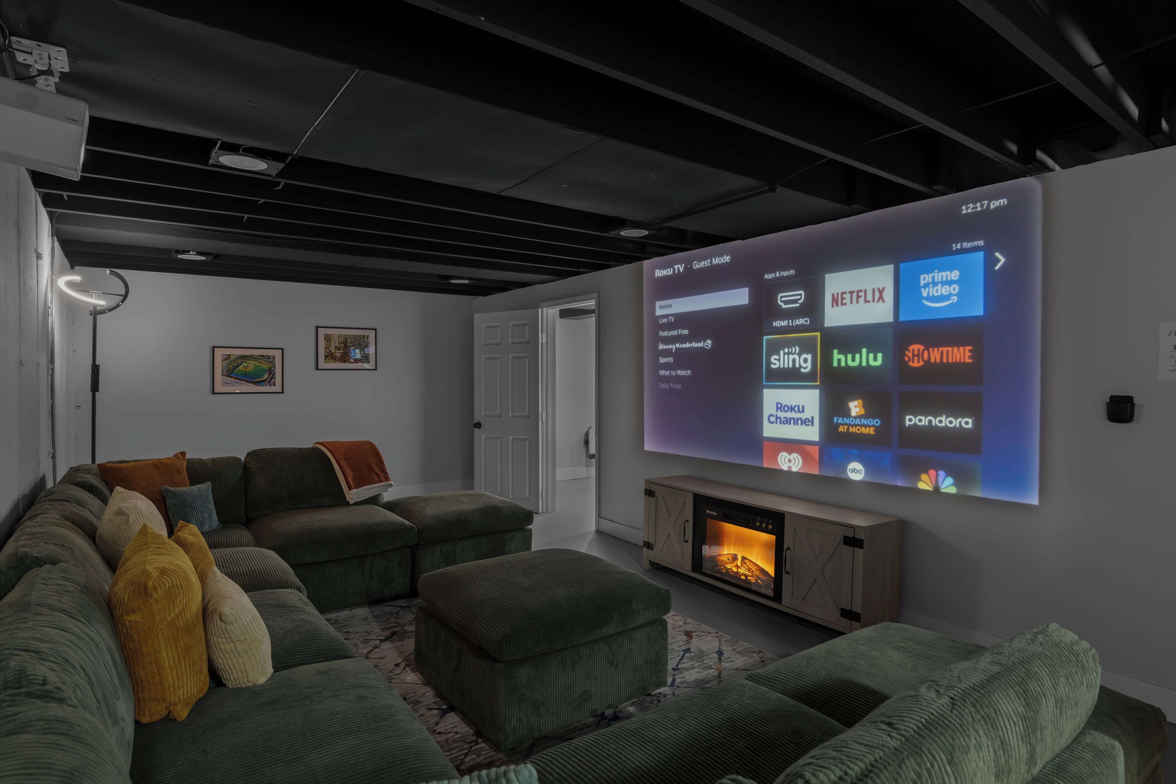 Ein modernes Wohnzimmer mit großem Flachbildfernseher, der eine Roku TV-Oberfläche anzeigt, einem Kamin und einem Ecksofa mit vielen Kissen.