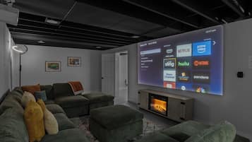 Ein modernes Wohnzimmer mit großem Flachbildfernseher, der eine Roku TV-Oberfläche anzeigt, einem Kamin und einem Ecksofa mit vielen Kissen.