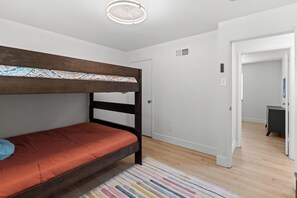 Ein Schlafzimmer mit Etagenbett, Holzboden, weißer Tür und Deckenleuchte.