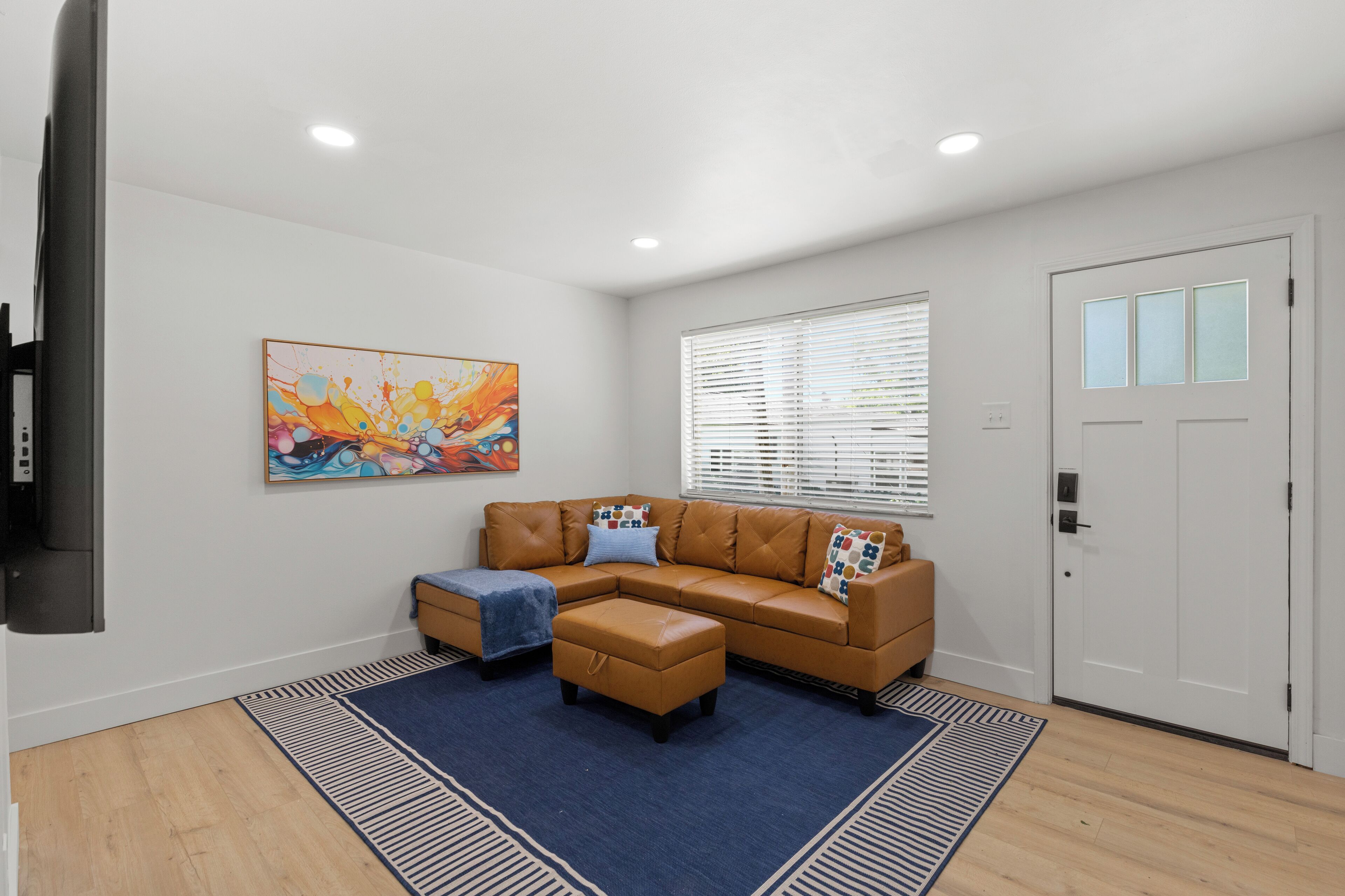 A living room with a sectional sofa, ottoman, and a blue rug.