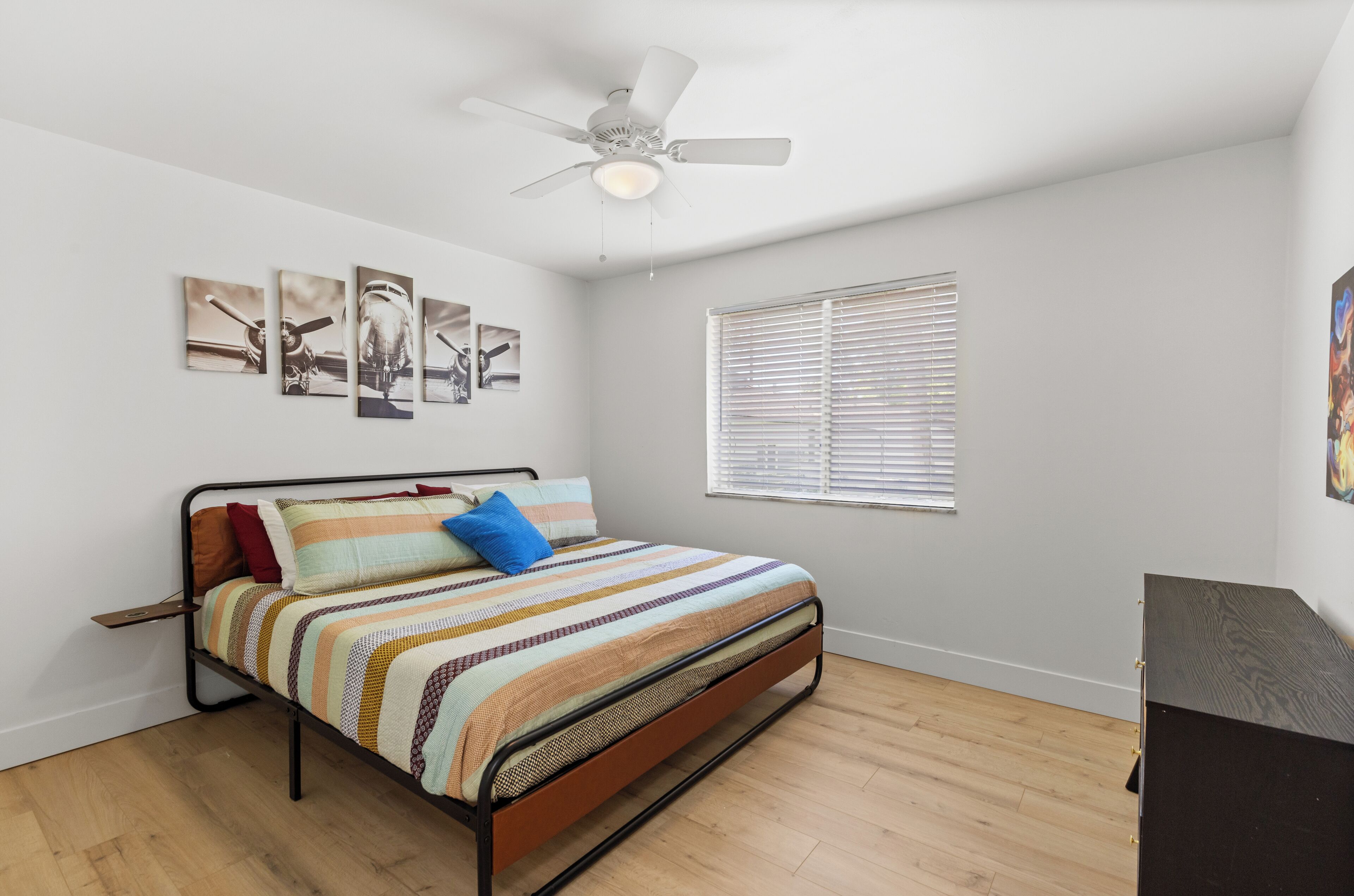 A bedroom with a bed, a ceiling fan, a window with blinds, and wall art.