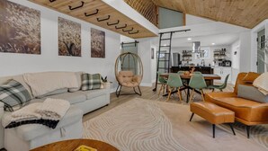 Een moderne woonkamer met een bank, stoelen, een eettafel en een keuken op de achtergrond.
