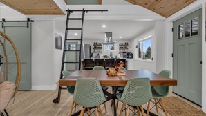 Een ruime eetruimte met een houten tafel en groene stoelen, een keuken op de achtergrond en een vide erboven.