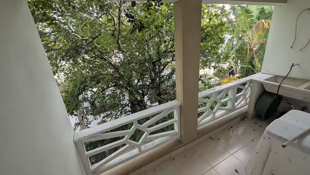 Un balcon doté d’une balustrade blanche, d’un sol carrelé et offrant une vue sur un feuillage verdoyant et luxuriant.