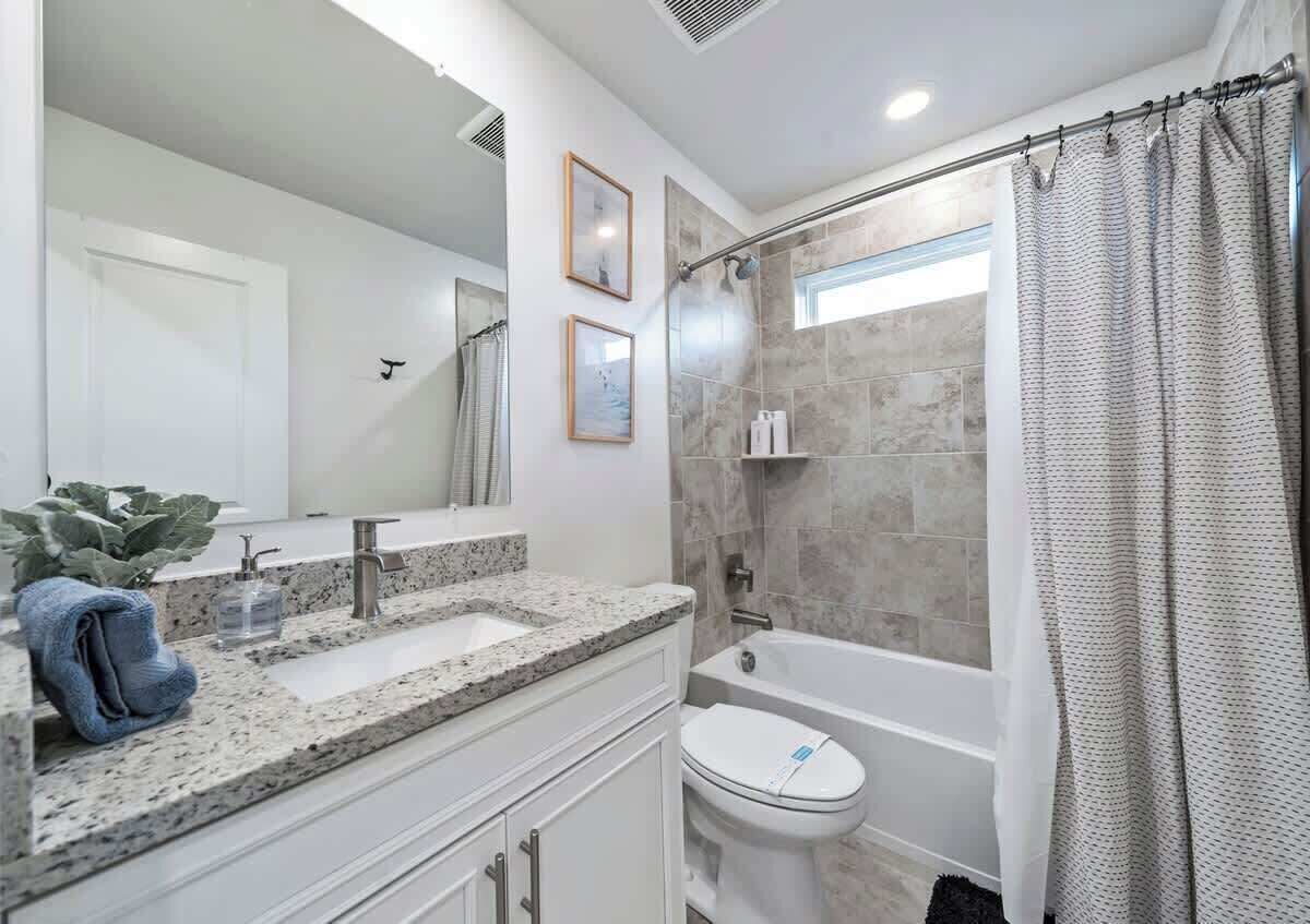 Une salle de bain moderne avec un lavabo surmonté d’un plan en granit, des toilettes blanches et un espace douche.