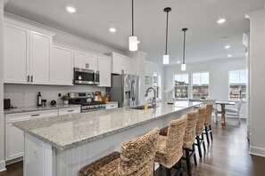 Una cocina moderna con armarios blancos, encimeras de granito y una isla central con taburetes de bar.