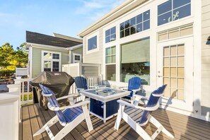 Eine Terrasse mit einem Glastisch, vier Adirondack-Stühlen, einem Grill und einem überdachten Bereich.
