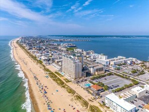 An aerial view of a coastal city with a long beachfront, high-rise hotels, and a marina. - The Sandy Hook Retreat| Grill & Sunroom (Ocean Pines)