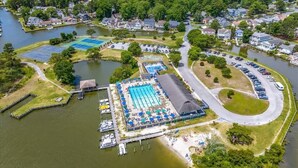 An aerial view of a lakeside community with a swimming pool, docked boats, and a parking area. - The Sandy Hook Retreat| Grill & Sunroom (Ocean Pines)