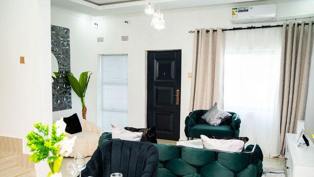Un salon moderne avec un canapé vert, une table à manger dressée pour quatre personnes et une porte noire.