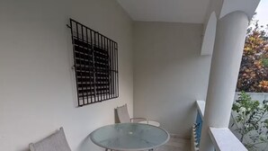 Un balcón con una mesa de vidrio y dos sillas, barandilla metálica y una ventana con rejas.