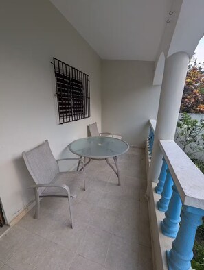 Ein Balkon mit Glastisch und zwei Stühlen, einem Metallgeländer und einem vergitterten Fenster.