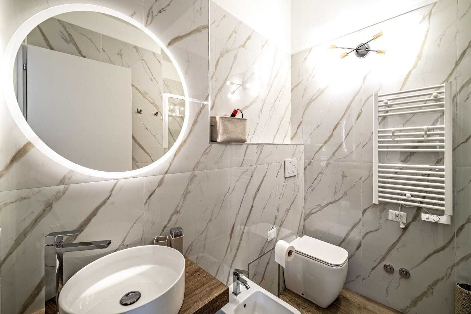 Un baño moderno con detalles de mármol en el salpicadero, un espejo redondo, un inodoro, un lavamanos y un perchero para toallas.