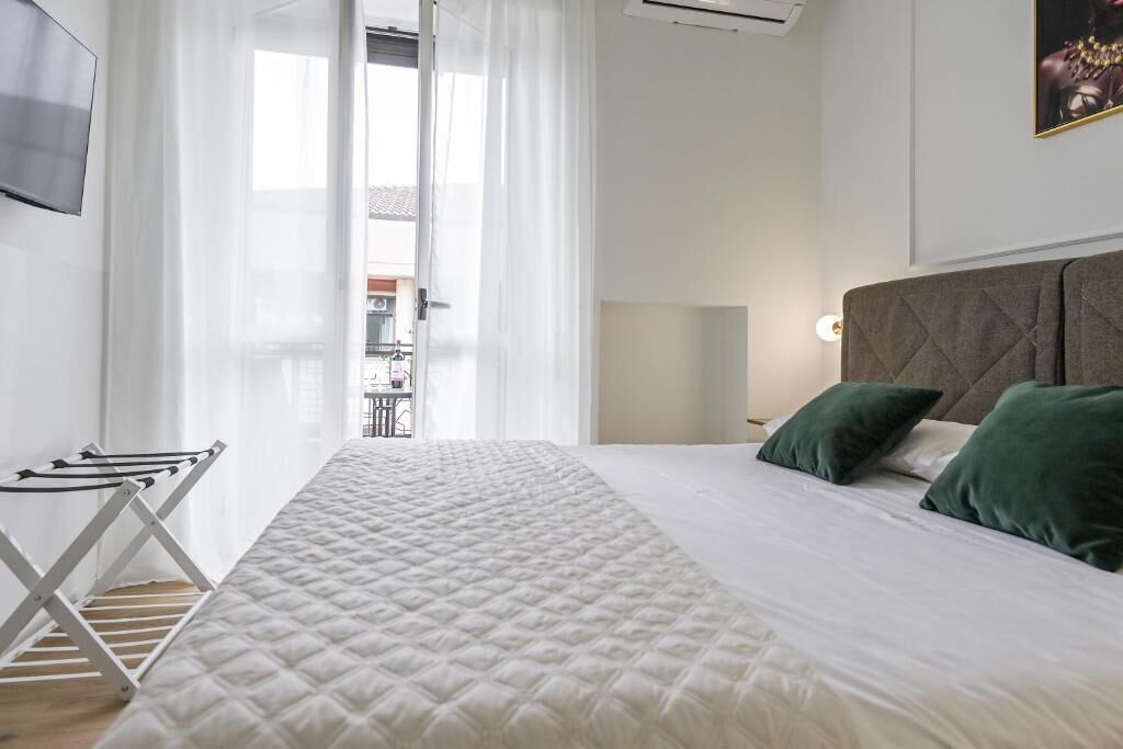 A neatly made bed with a quilted cover, a bedside lamp, and green pillows.