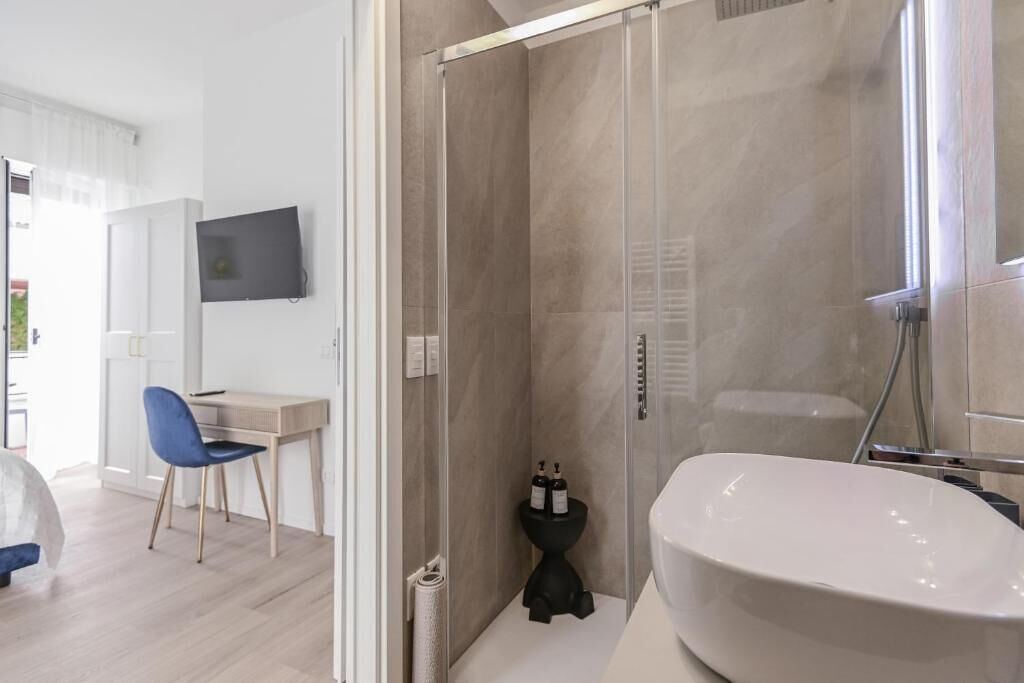 A modern bathroom with a glass-enclosed shower, a white sink, and a small black toilet.