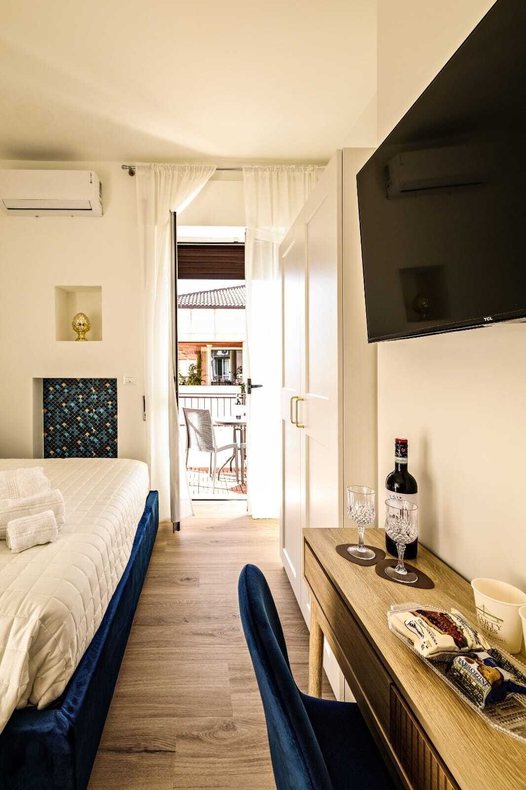 Habitación de hotel con cama, escritorio, botella de vino, copas y bandeja de aperitivos.