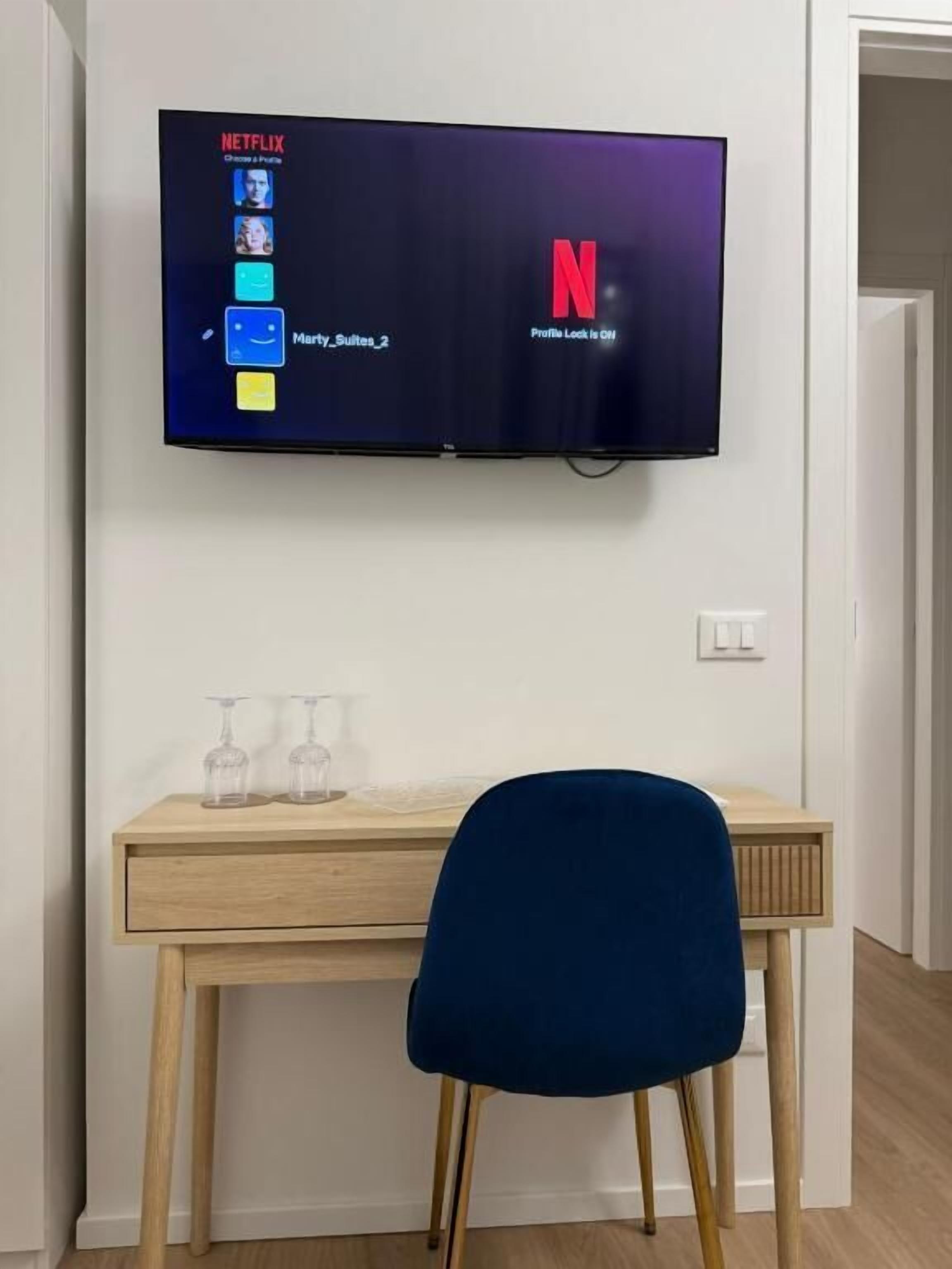 A flat-screen TV mounted on a wall displaying the Netflix interface with a profile named "Mary_Sultes_2".