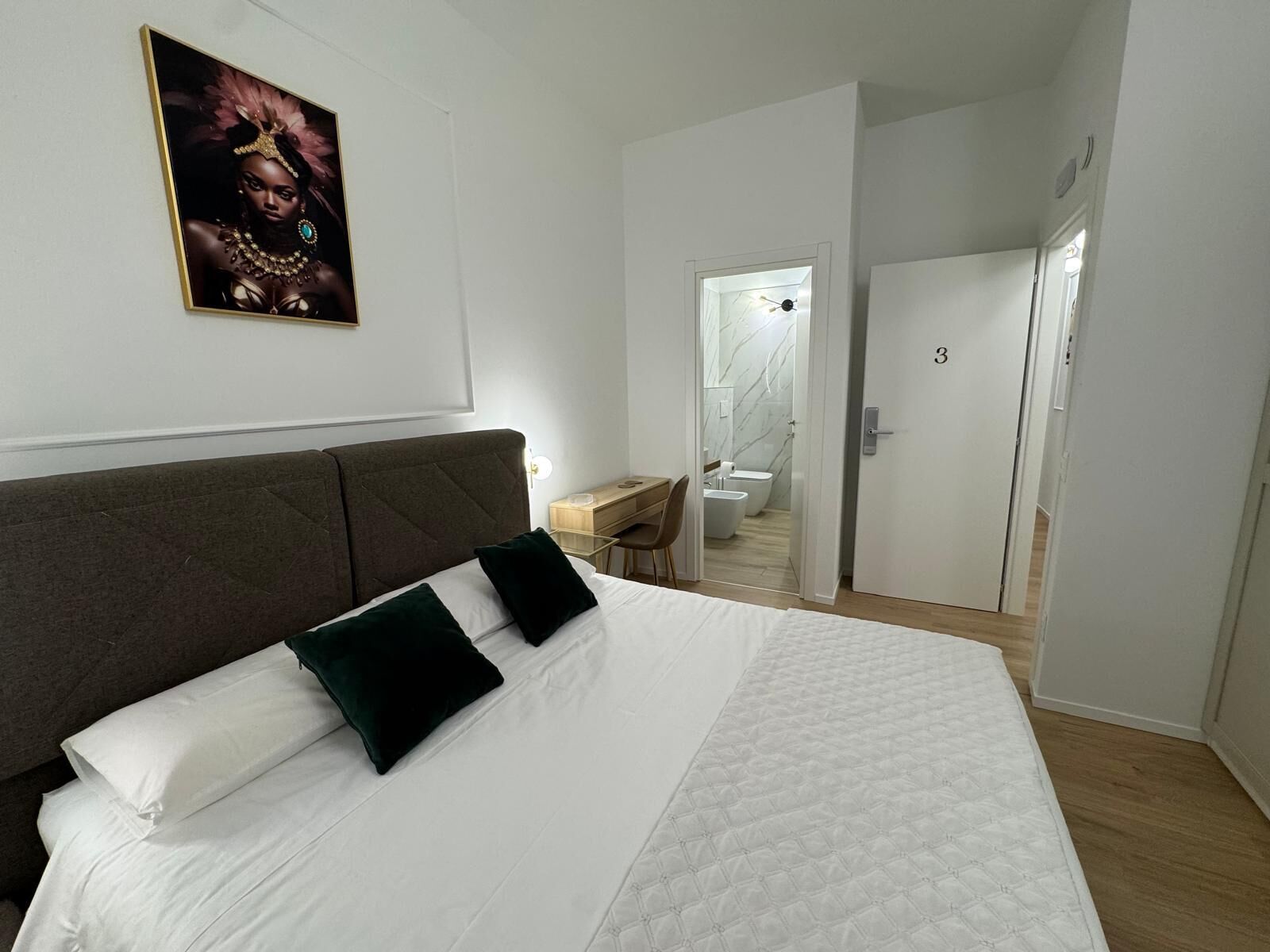 Une chambre à coucher avec un grand lit, un bureau et une salle de bain visible à travers une porte ouverte.