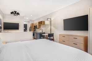A modern hotel room with a large bed, a flat-screen TV, a desk with a chair, and a kitchenette. - XStay Suites Mansfield (Mansfield)