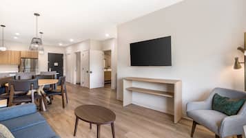 Ein modernes Wohnzimmer mit einer Couch, einem Couchtisch, einem an der Wand befestigten Fernseher und einem Essbereich mit Stühlen und einem Tisch.