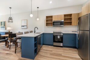 A modern kitchen with a central island, built-in microwave, oven, and refrigerator. - XStay Suites Mansfield (Mansfield)