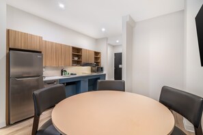 A modern kitchen with a built-in refrigerator, microwave, and wooden cabinets. There is a dining table with chairs and a small island with a sink. - XStay Suites Mansfield (Mansfield)