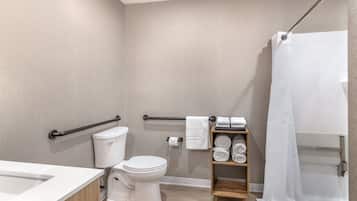 Un baño moderno con inodoro, ducha con cortina, estante de madera con toallas y barra de apoyo.